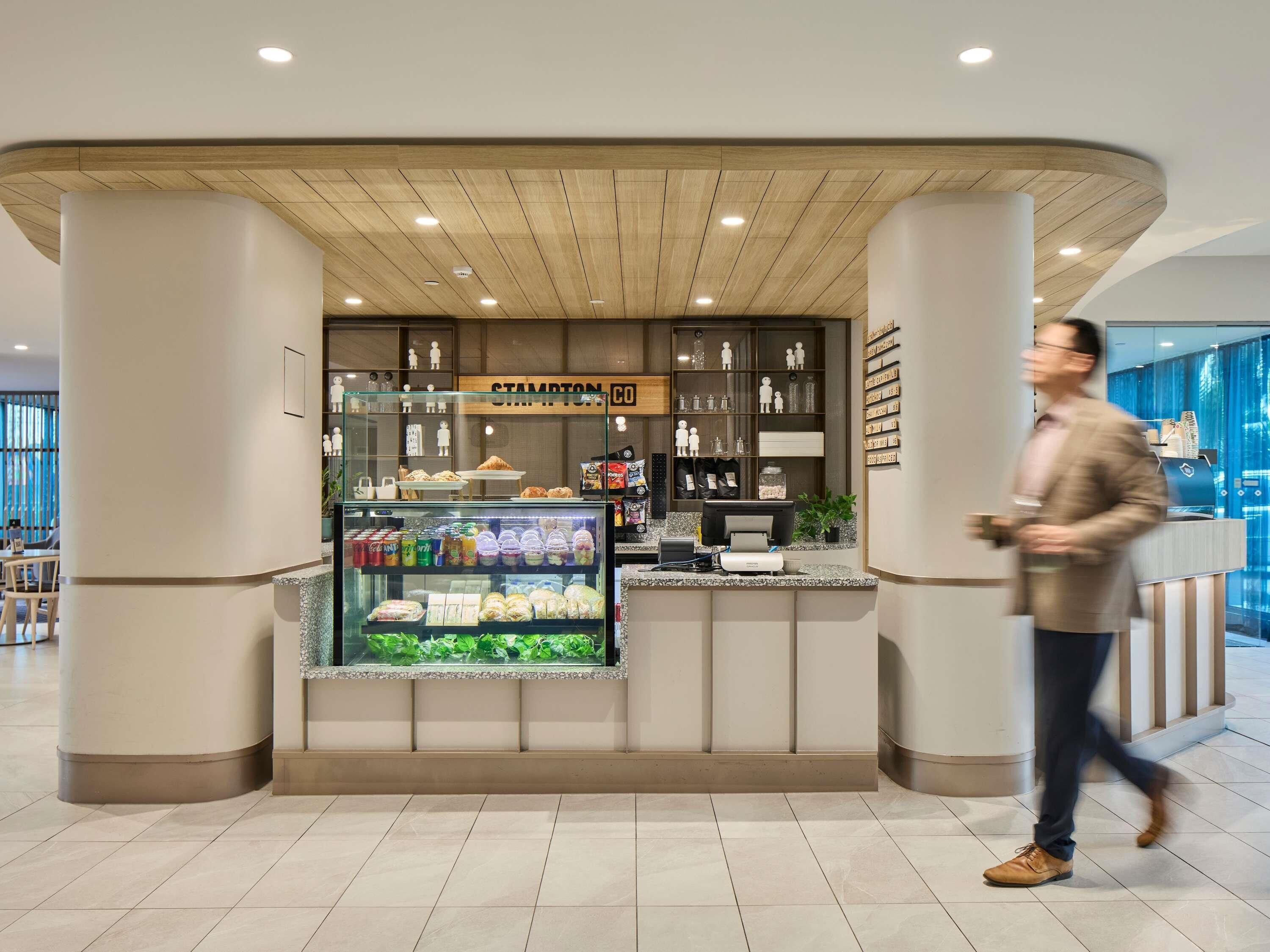 Een modern café met een glazen vitrine, een houten plafond en een bord met de tekst 'STAMPTON COFFEE'.