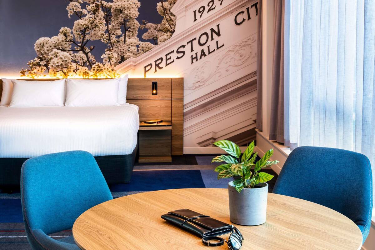 Una habitación de hotel con cama, mesita de noche, escritorio y una planta en maceta.