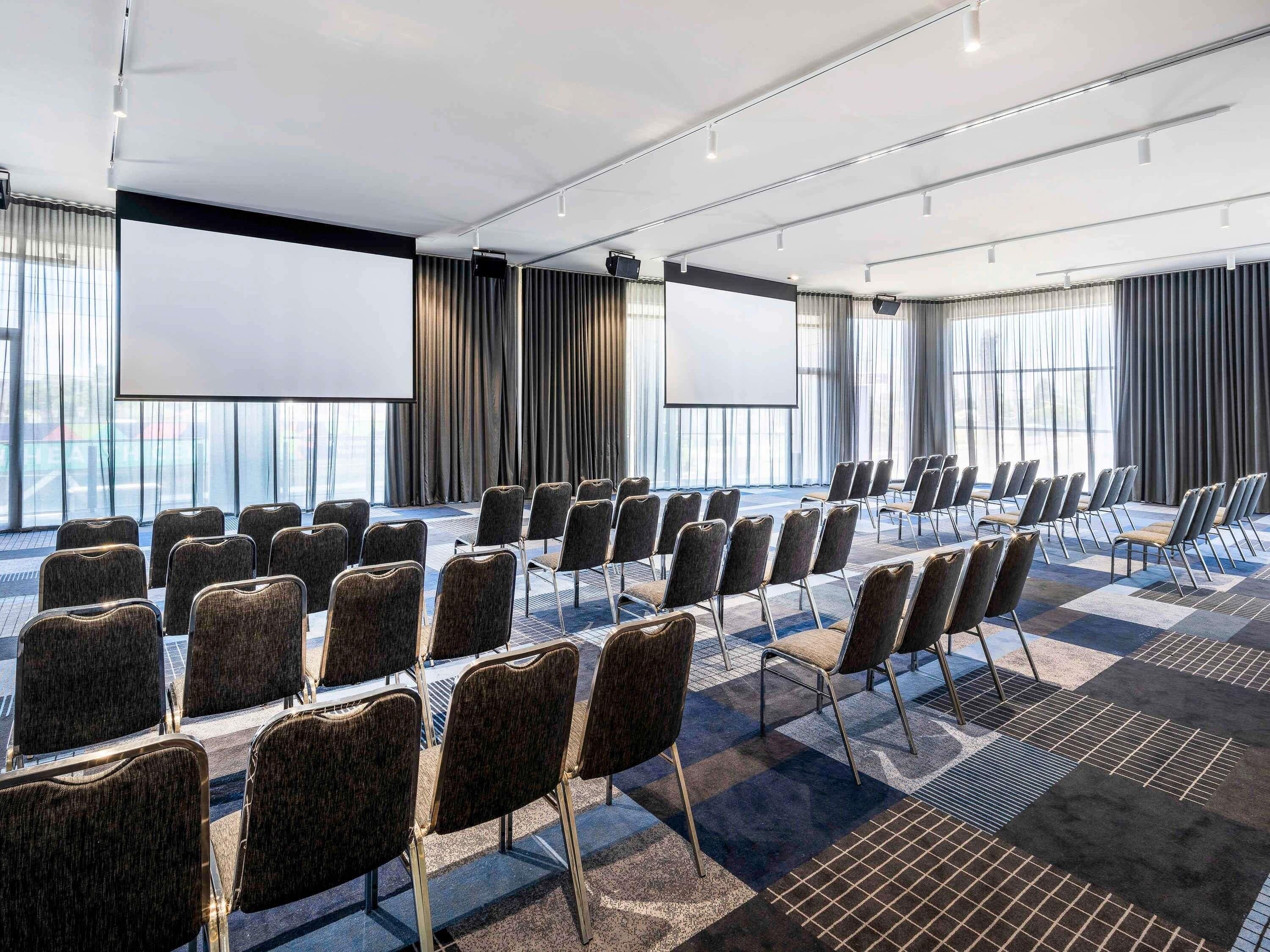 A conference room with rows of chairs, a large screen, and a view of the city through large windows.