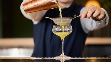 A bartender pouring a yellow liquid into a martini glass using a strainer.