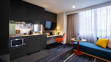 Une chambre d’hôtel compacte comprenant un coin cuisine, un espace repas, un canapé et un téléviseur.