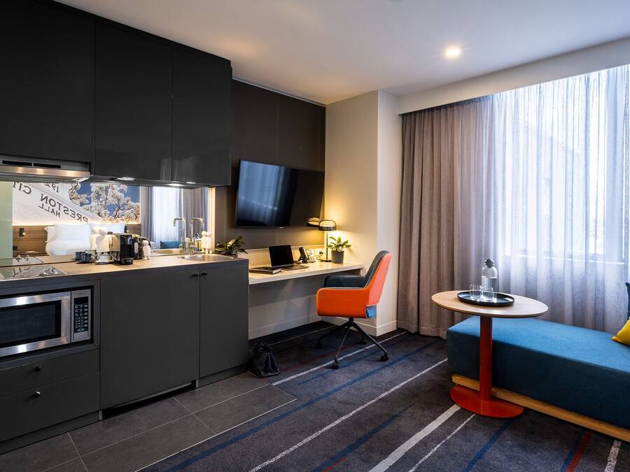 Ein kleines Hotelzimmer mit Küchenzeile, Essbereich, Sofa und Fernseher.