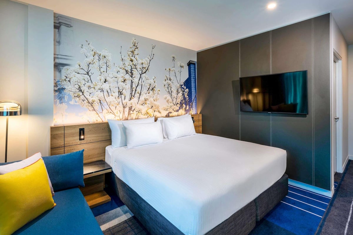 Una habitación de hotel moderna con una cama grande, un televisor de pantalla plana, una mesita de noche y un televisor montado en la pared.