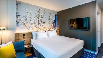 Una habitación de hotel moderna con una cama grande, un televisor de pantalla plana, una mesita de noche y un televisor montado en la pared.