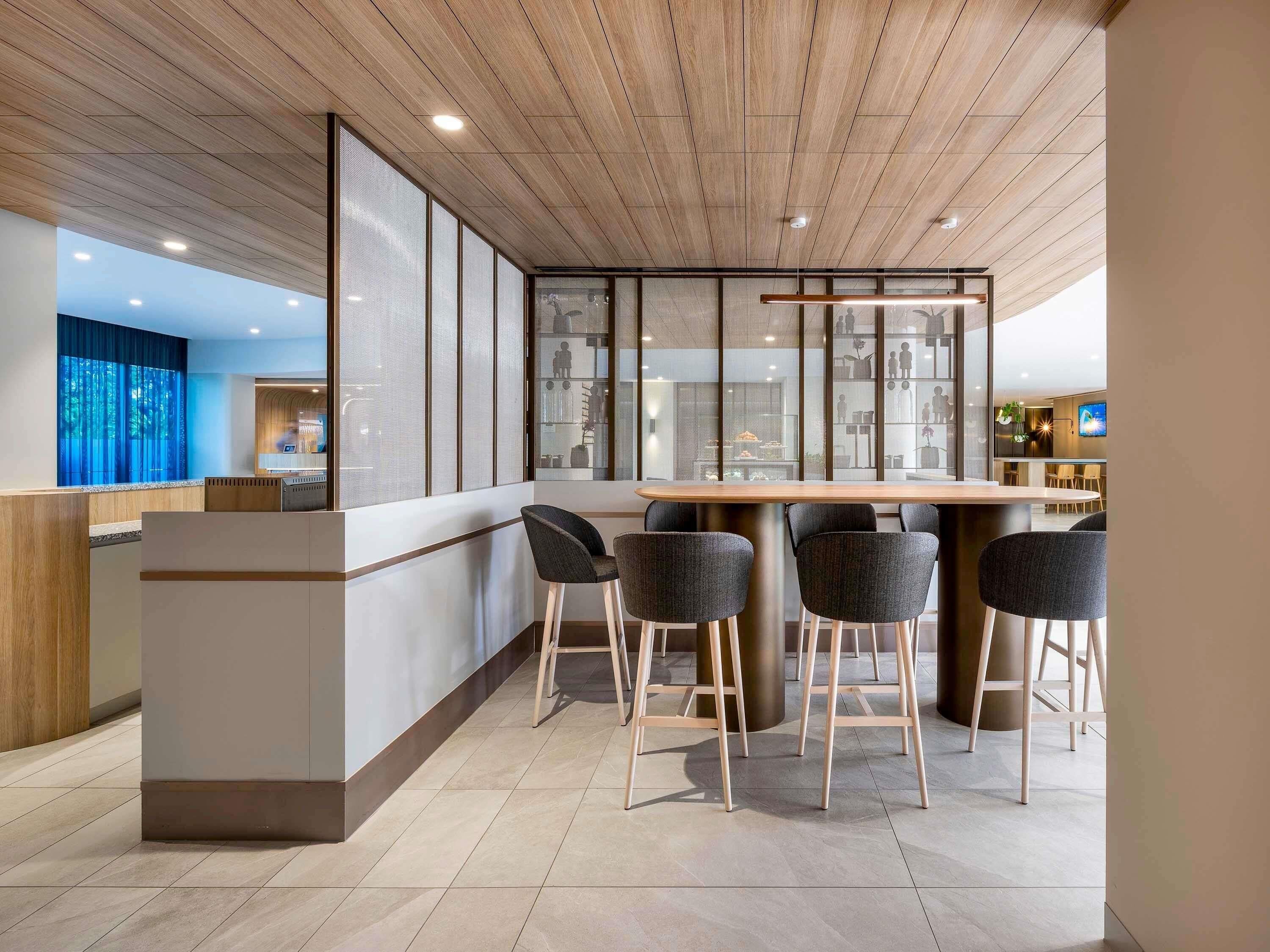 Uma área de bar moderna com teto de madeira, um balcão longo e quatro banquetas.