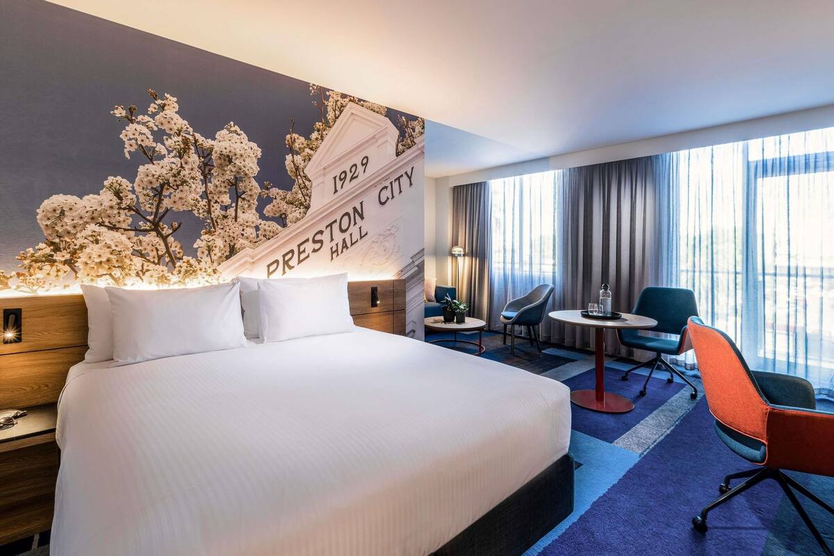 Habitación de hotel con una cama grande, un escritorio, una silla y un letrero en la pared que dice 'PRESTON CITY HALL 1929'.
