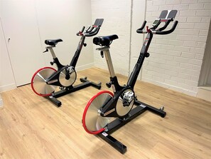 Two stationary bikes in a room with wooden flooring and white brick walls. - Novotel Melbourne Preston (Preston)