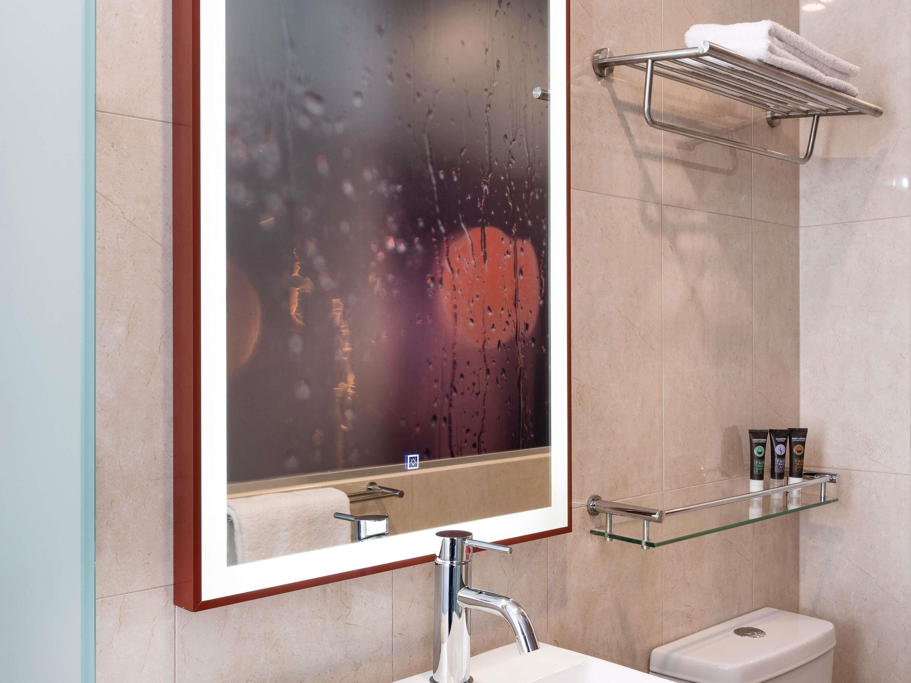 A bathroom with a mirror, a sink, a toilet, a towel rack, and a glass shelf with toiletries.