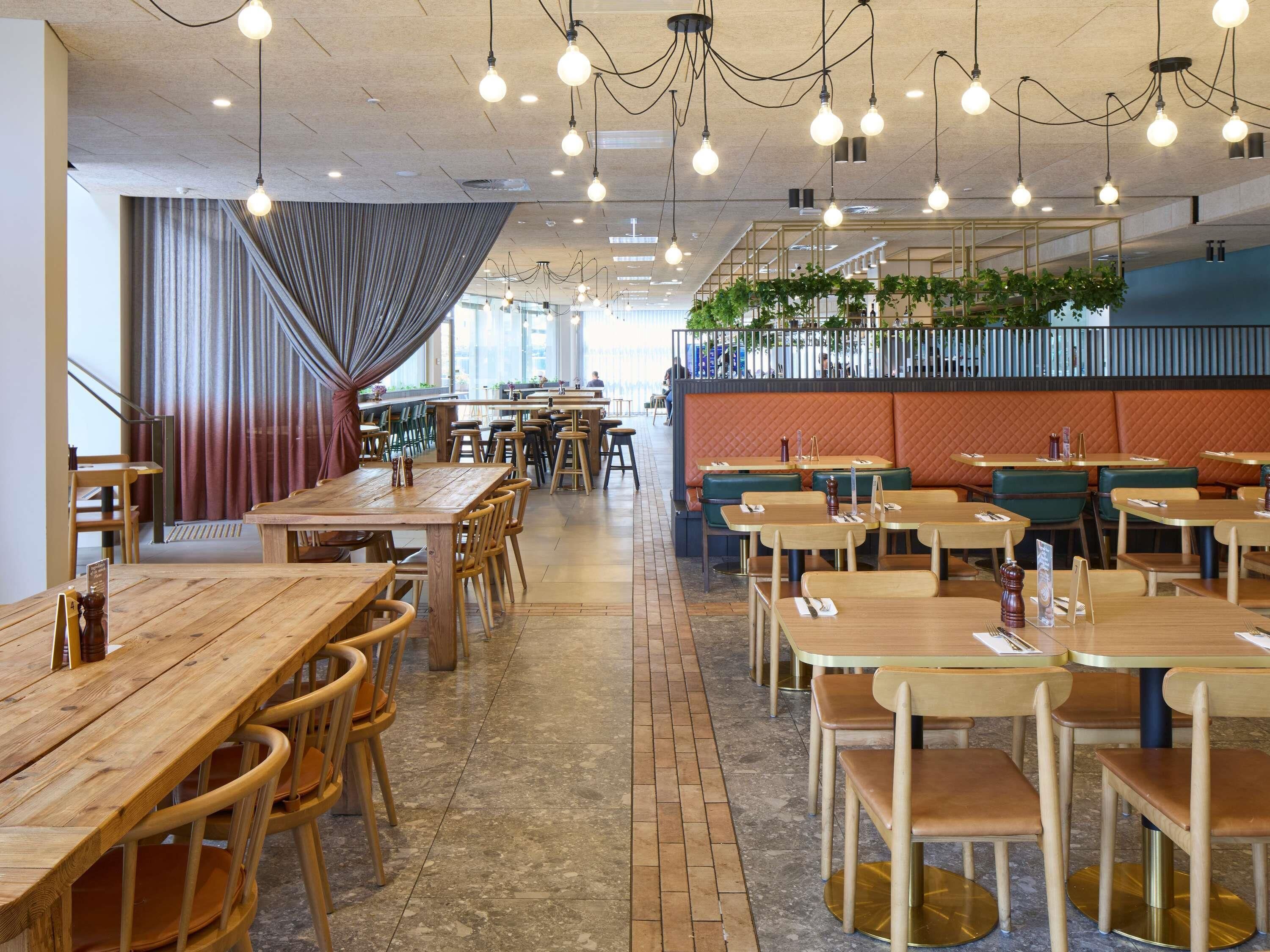 En restaurant med træborde og stole, hængende lyspærer og en murstensgulv.