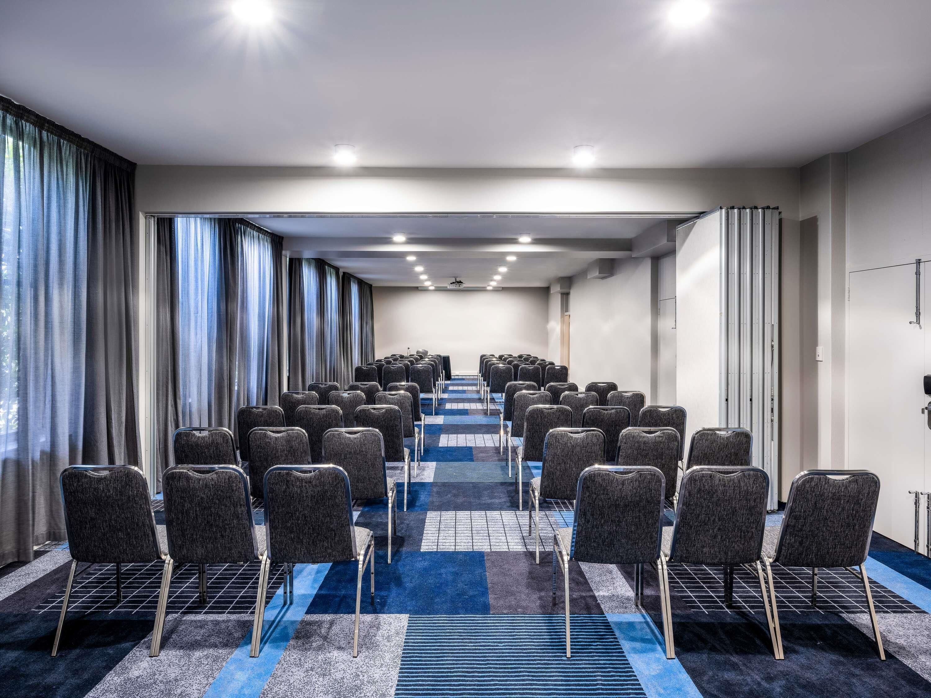 A conference room with rows of chairs, a carpeted floor, and a window with curtains.