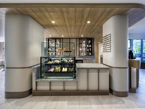 A modern cafe with a glass display case of pastries, wooden ceiling, and a menu on the wall. - Novotel Melbourne Preston (Preston)