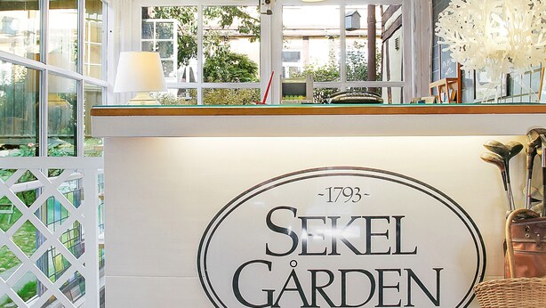 Vastaanottoalue, jossa on kyltti, jossa lukee ”SEKEL GARDEN HOTEL”, ja josta on näkymä ulos.