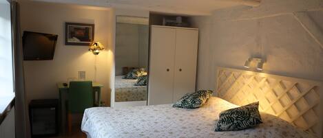A bedroom with a bed, a desk, a chair, a wardrobe, and a mirror.