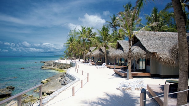 A beachside resort with thatched-roof huts, lounge chairs, and a clear view of the ocean.
