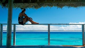 A person sitting on a wooden deck with a view of turquoise ocean water.