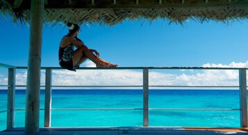 Una persona sentada en una terraza de madera con vista al agua turquesa.