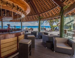 Un bar frente a la playa con mobiliario de mimbre y vista al océano.