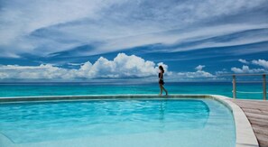 A person walking along a poolside with a view of the ocean and clouds.