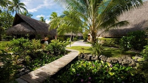 A tropical resort with thatched-roof huts, a wooden pathway, and lush greenery.