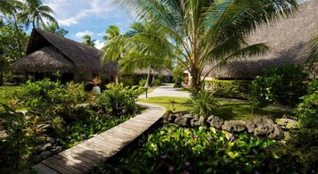Un resort tropical con cabañas de techo de paja, un sendero de madera y abundante vegetación.