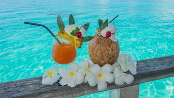 A tropical drink and a coconut with flowers on a wooden railing by a clear blue pool.