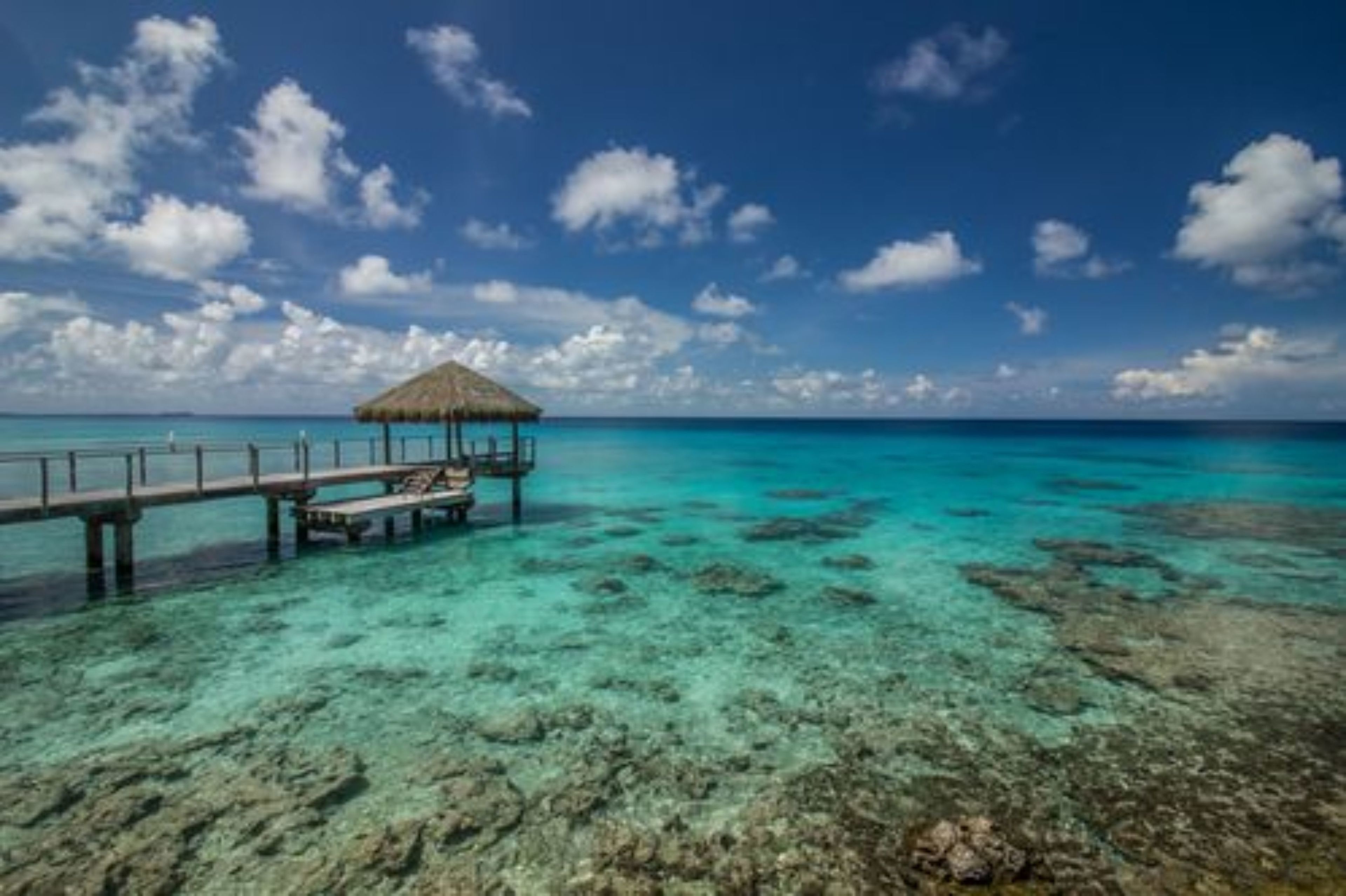 A pier extending into turquoise waters with a thatched-roof structure at the end.