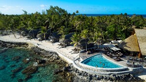 A resort with a pool surrounded by palm trees and a view of the ocean.