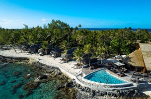 Un resort con piscina rodeada de palmeras y vista al océano.