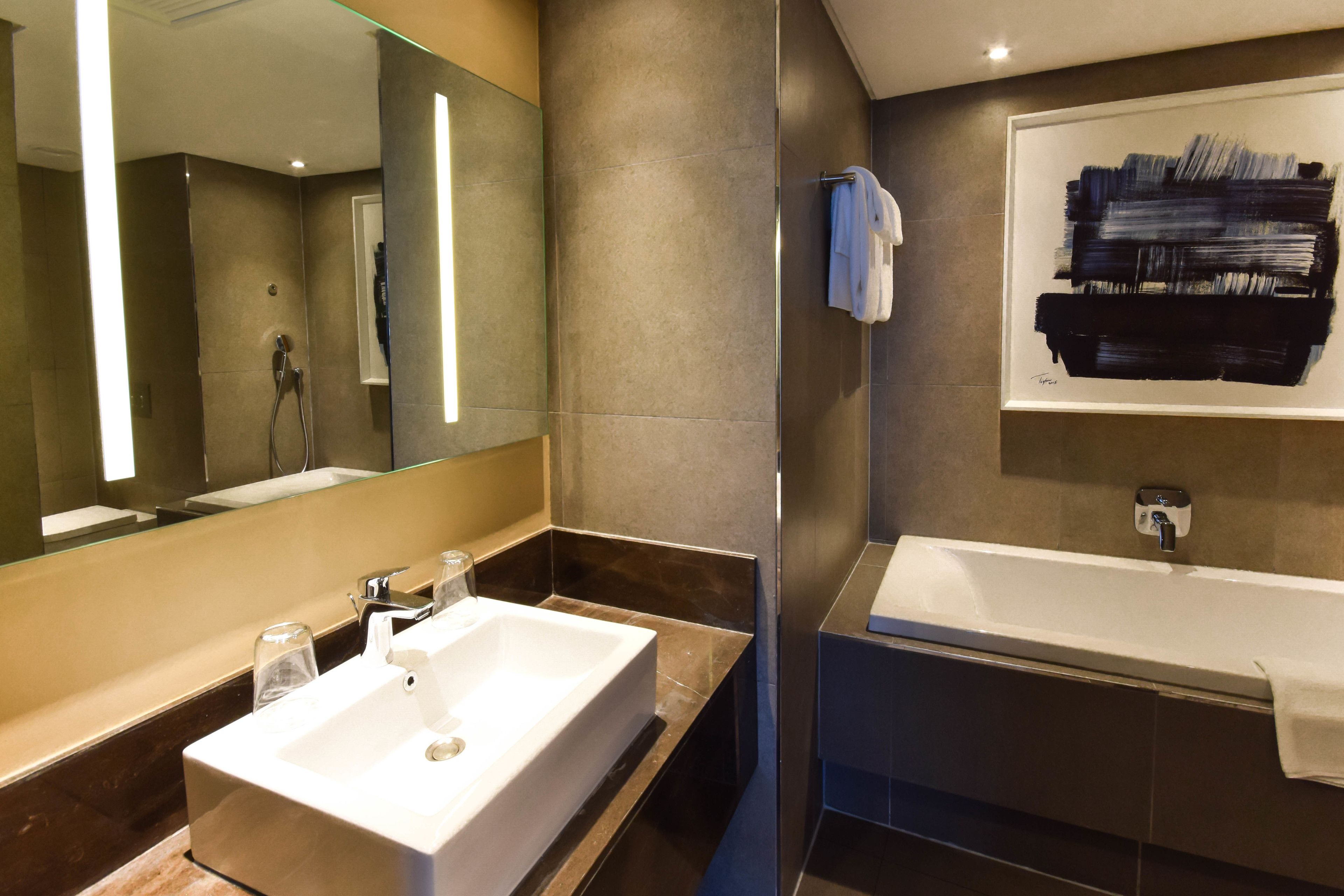 Een moderne badkamer met een grote spiegel, een witte wastafel en een bad.