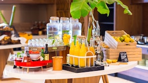Mesa de buffet com diversos alimentos, bebidas e um vaso de planta.
