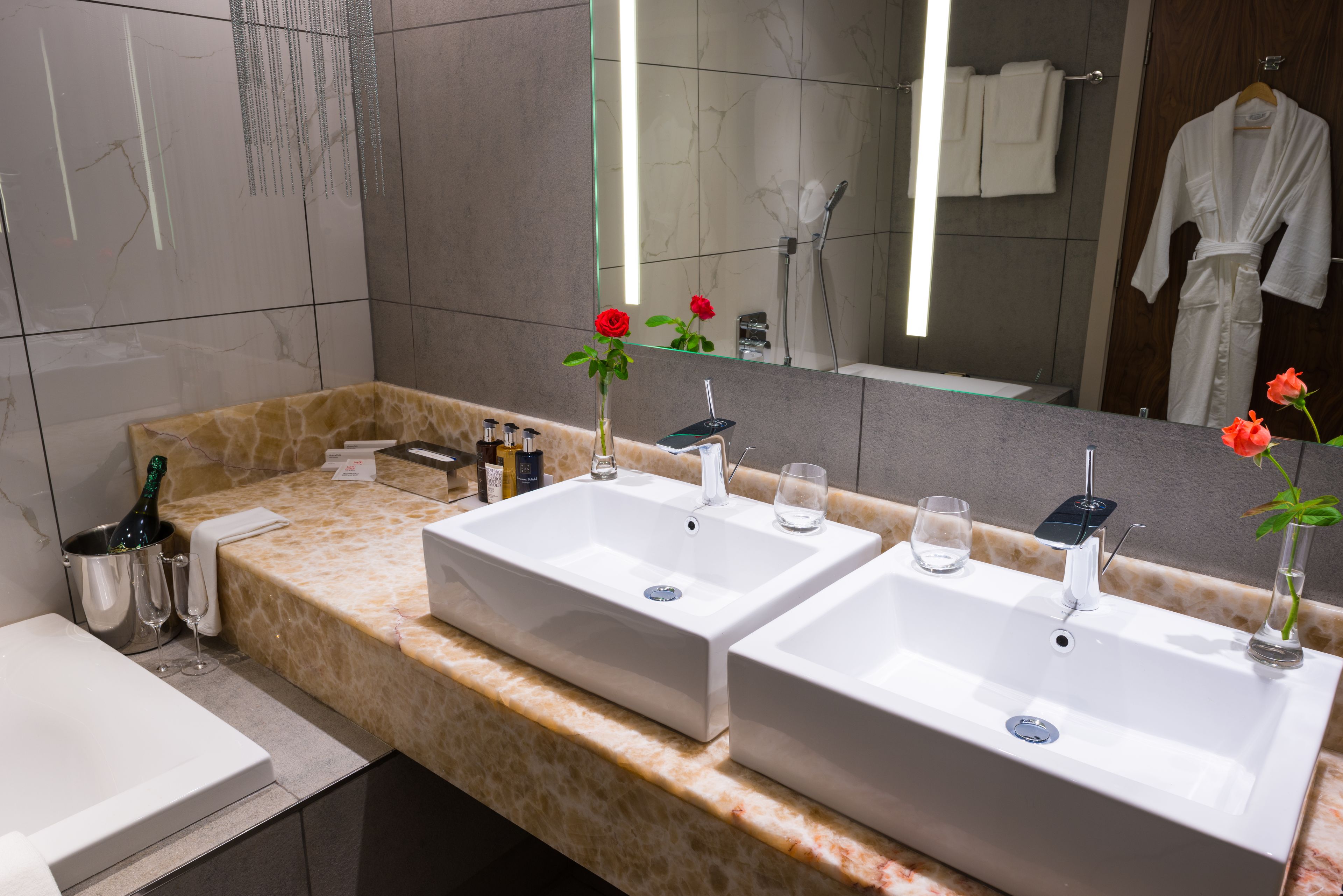 A bathroom with two sinks, a bathtub, a vanity with toiletries, and a large mirror.