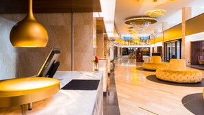 Um lobby moderno com uma receção de mármore, uma grande luminária pendente dourada e um candelabro central.