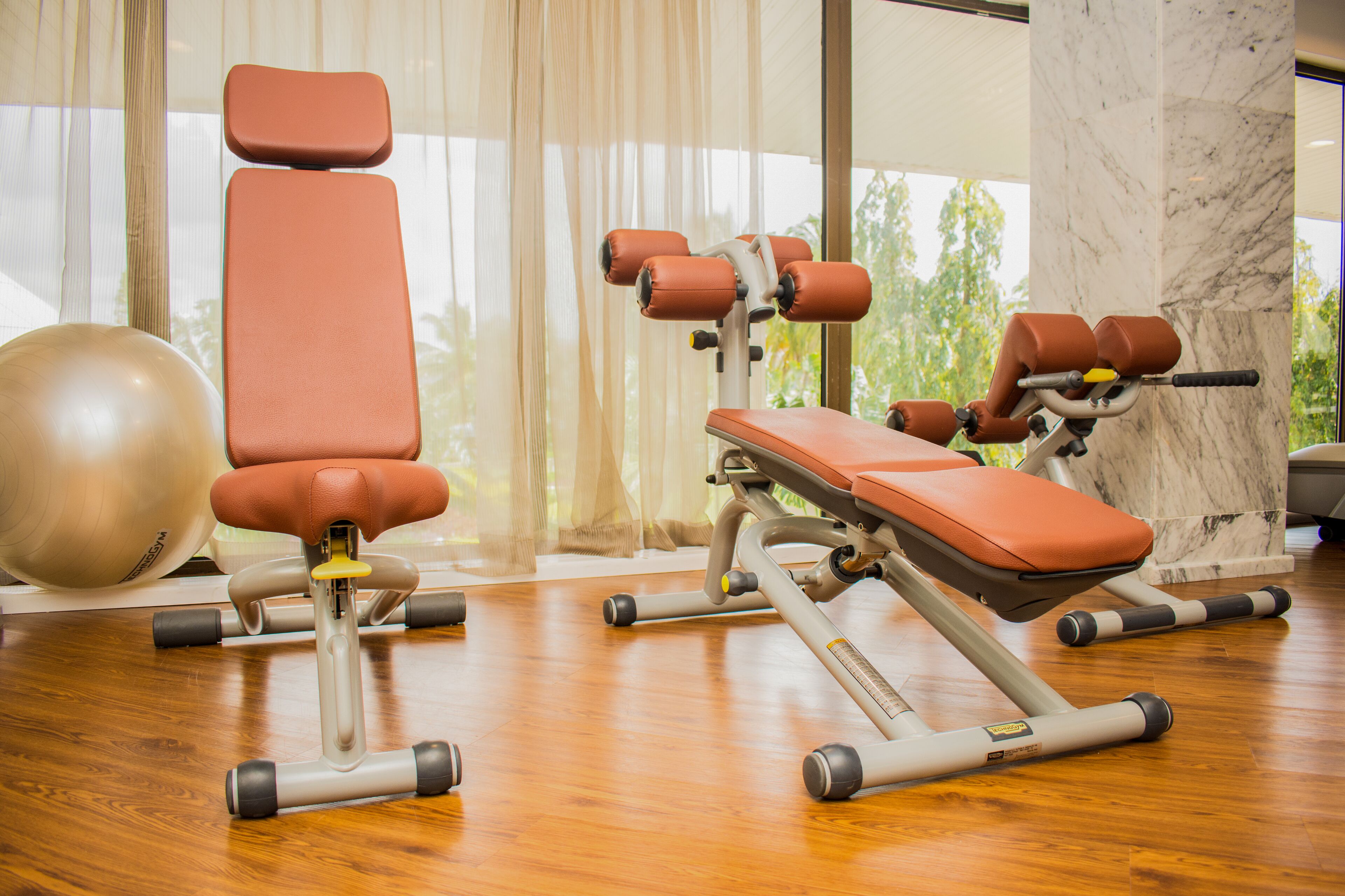 A gym with exercise equipment, a large exercise ball, and a view of greenery through the window.