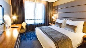 A hotel room with a large bed, a desk, a chair, a TV, and a window with curtains.