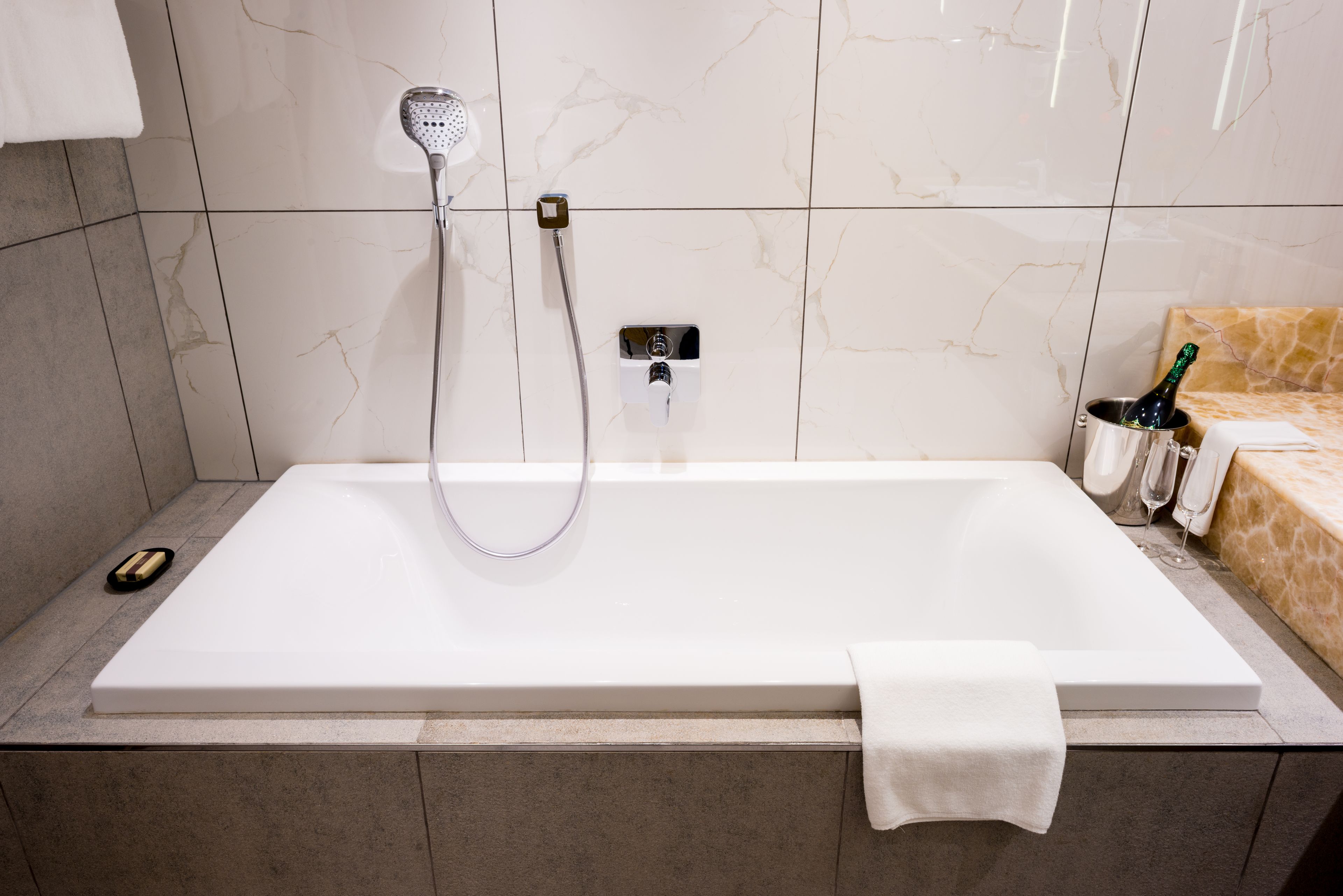 A modern bathroom with a large bathtub, a handheld showerhead, and a bottle of champagne.