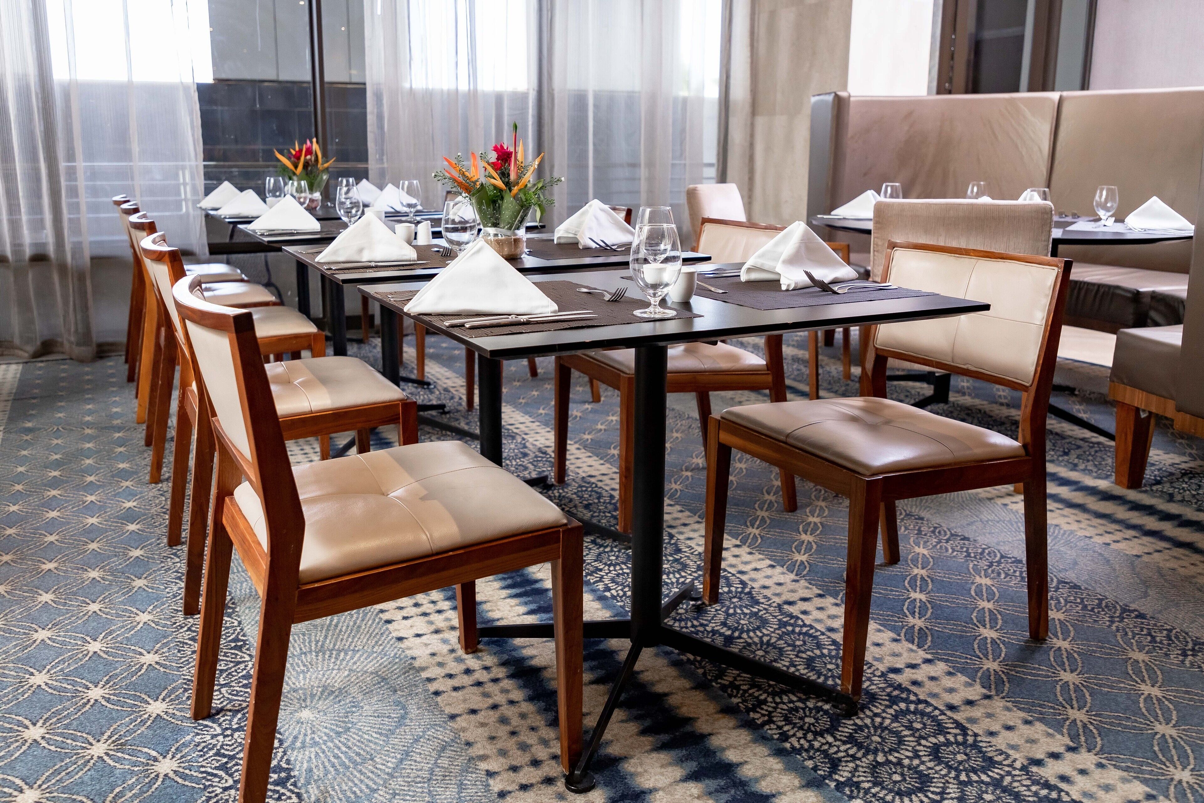 A dining area with tables set for service, chairs, and a patterned carpet.