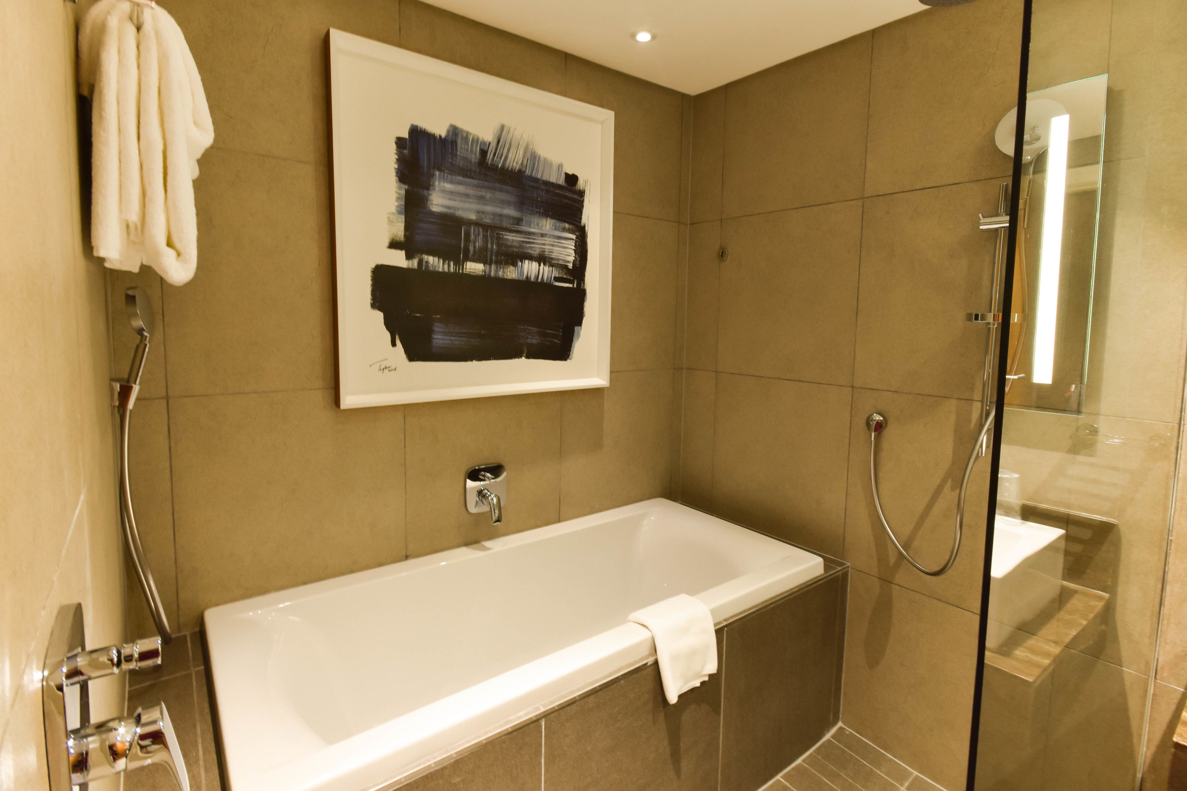A modern bathroom with a bathtub, a glass shower enclosure, and a framed abstract painting on the wall.