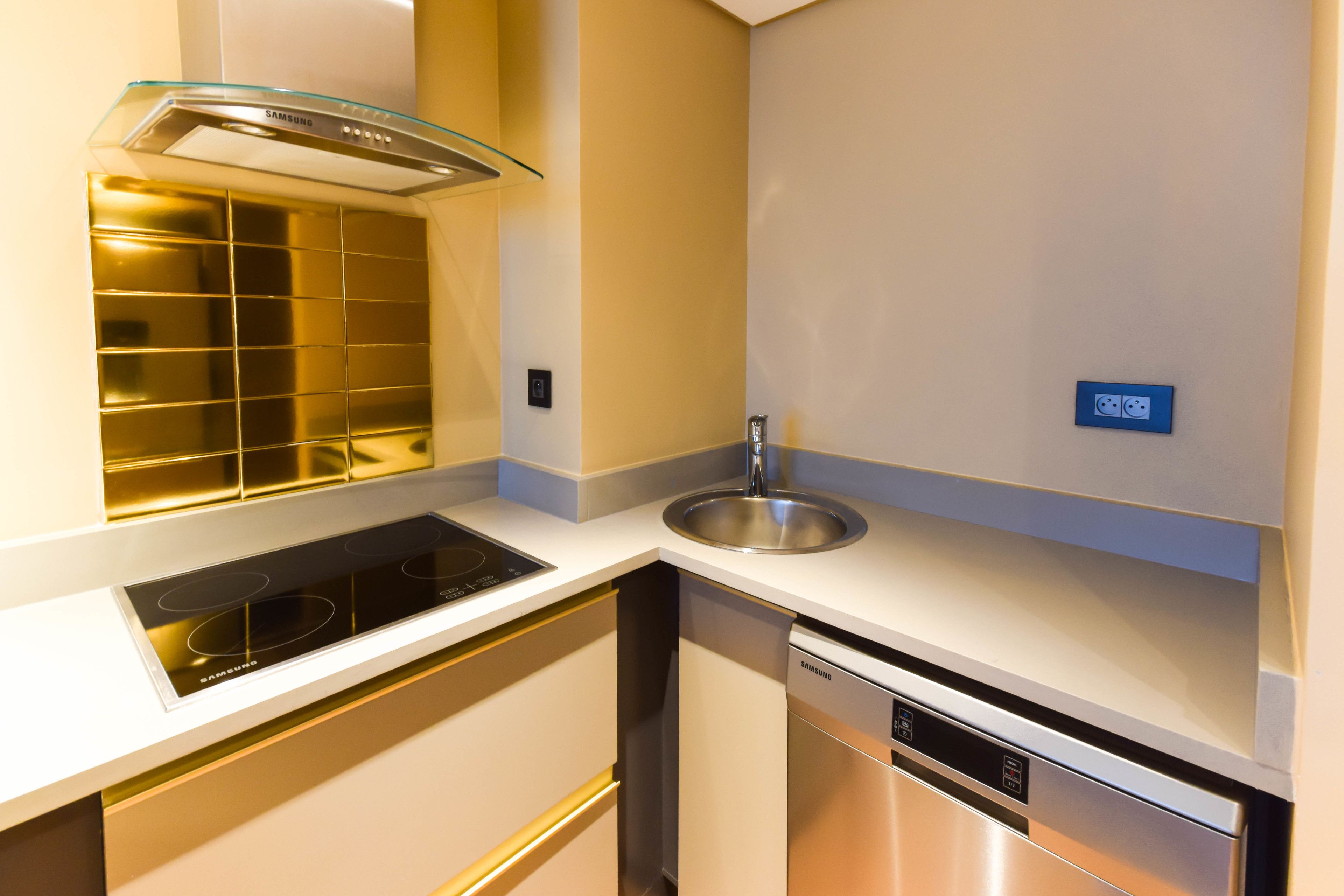 A modern kitchen with a built-in stove, a glass range hood, a stainless steel sink, and a dishwasher.
