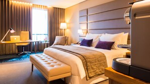 Quarto de hotel com uma cama grande, uma escrivaninha com um laptop, uma máquina de café e vista para o exterior.