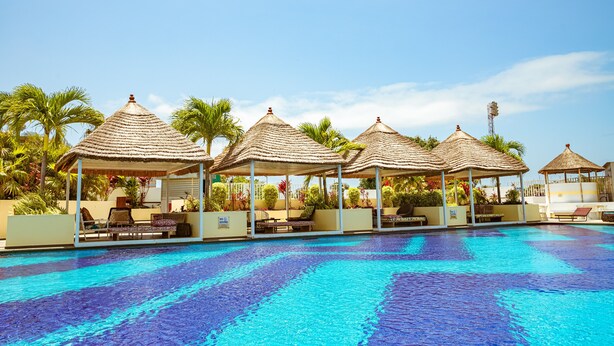 Uma piscina com espreguiçadeiras e palafitas cobertas de palha.
