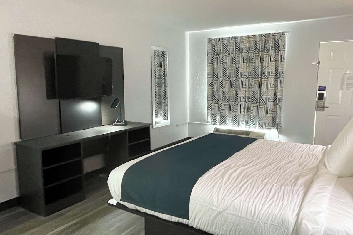 Hotelkamer met een bed, een bureau met stoel, een flatscreen televisie en gordijnen met dessin.