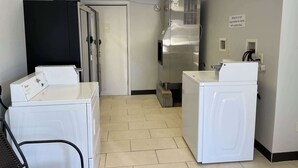 Une buanderie équipée de deux machines à laver blanches, d’un grand sèche-linge en acier inoxydable et d’une porte donnant sur une autre pièce.