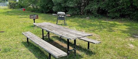 A picnic table with benches in a grassy area with trees in the background.