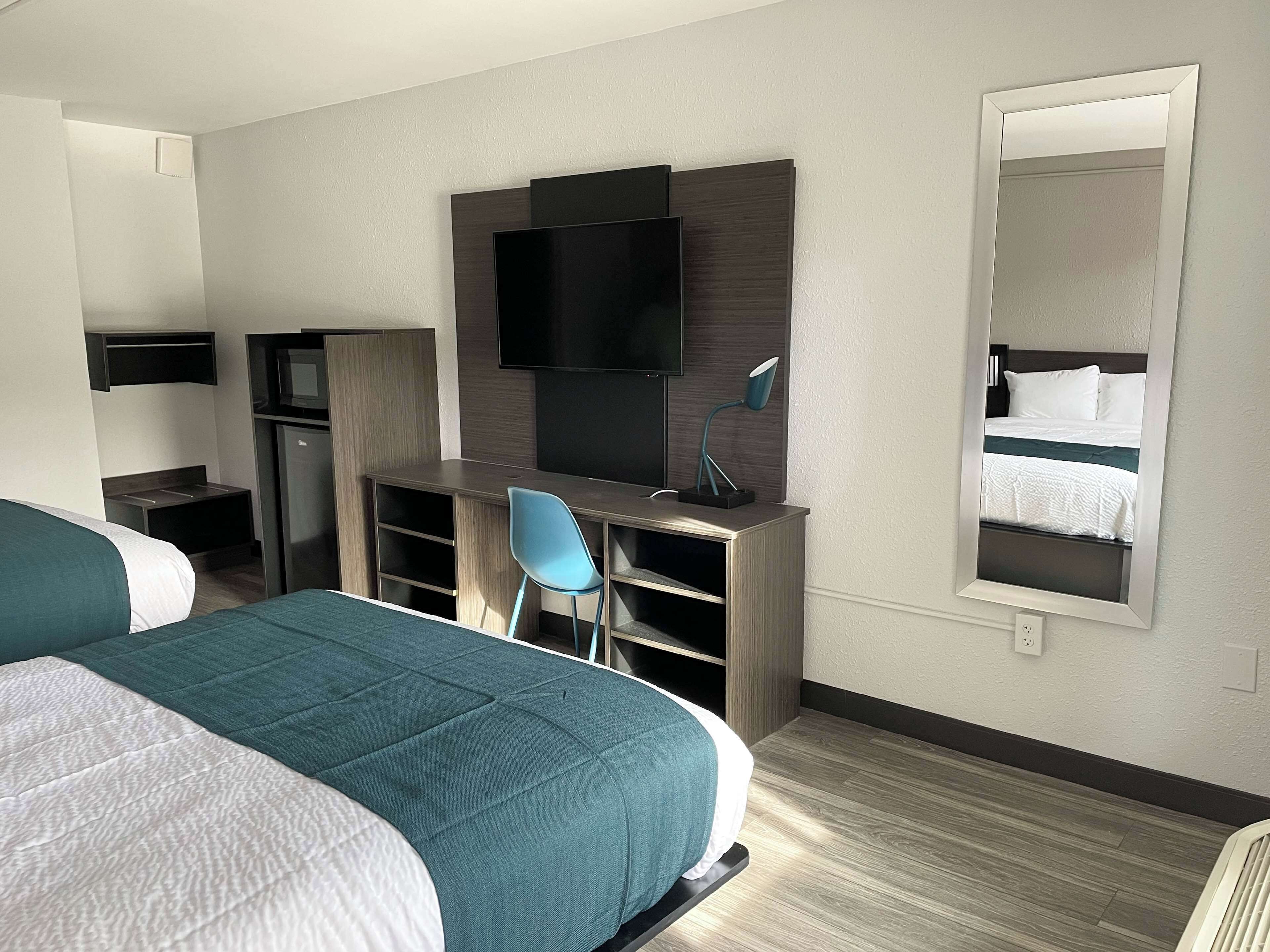Habitación de hotel con dos camas, un escritorio con silla, un televisor y un espejo.