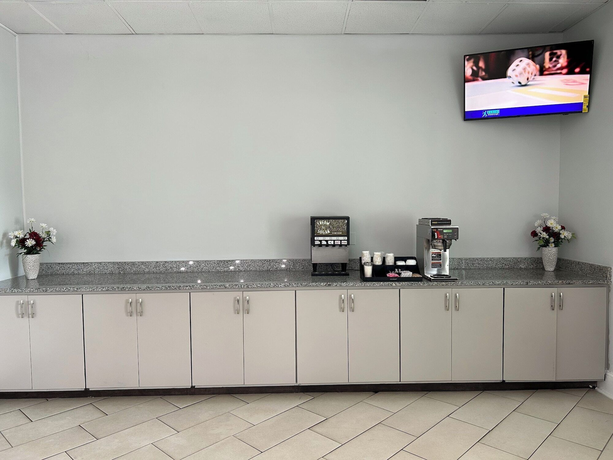 A clean, modern kitchen area with a coffee machine, a display case, and a television mounted on the wall.