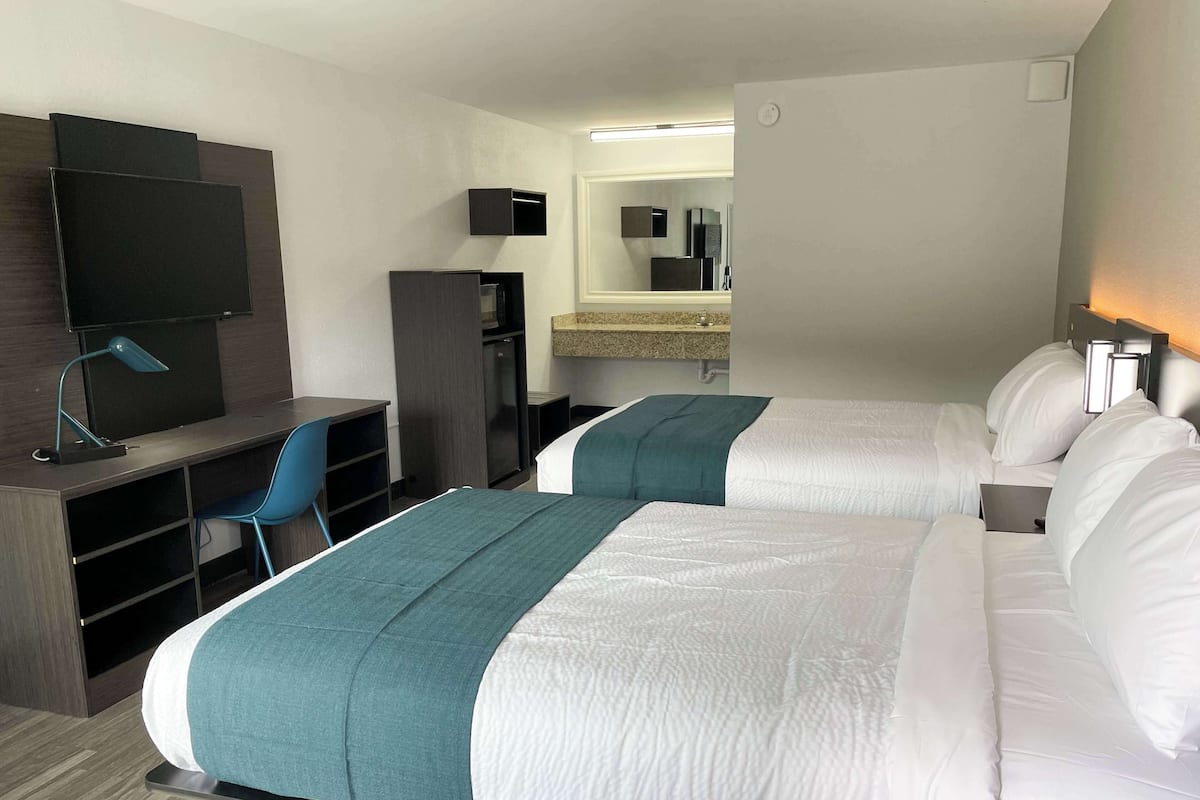 Een hotelkamer met twee bedden, een bureau, een stoel, een televisie en een spiegel.