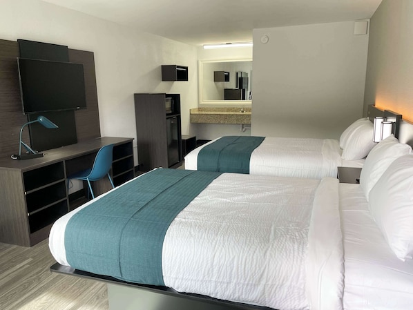 Quarto de hotel com duas camas, uma escrivaninha, uma cadeira, uma televisão e um espelho.