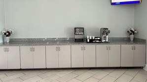 Un espace d’accueil propre et moderne, doté d’une machine à café, d’un écran numérique et de quelques fleurs décoratives.