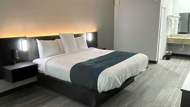 Une chambre d’hôtel moderne, dotée d’un grand lit, de tables de chevet, d’une petite table et d’une salle de bain visible à travers une porte ouverte.