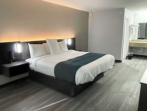 Quarto de hotel moderno com uma cama grande, mesas de cabeceira e um banheiro visível através de uma porta aberta.